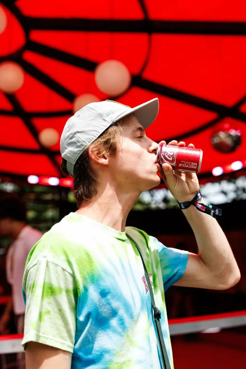 A festival-goer drinking a Coca-Cola under the red canopy