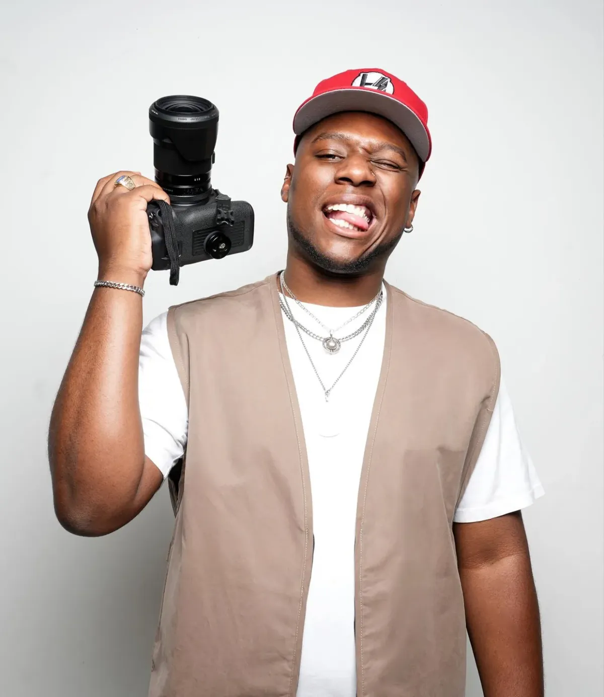Herc grinning with his camera on his shoulder, in a red cap